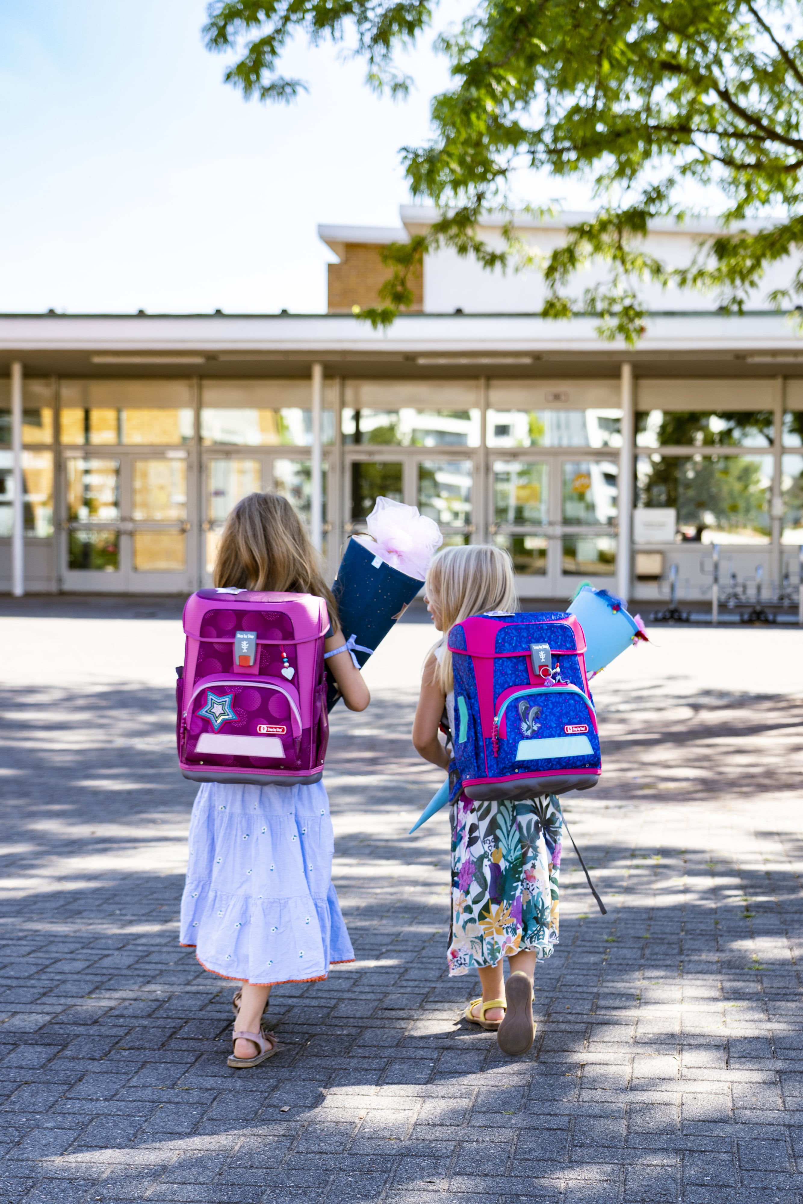 Zwei junge Mädchen laufen mit ihren Schulranzen und Schultüten auf den Eingang der Grundschule zu.