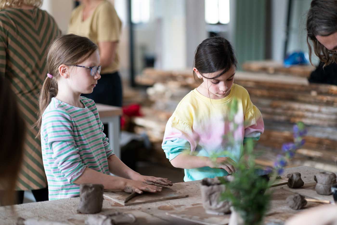 Zwei Mädchen kneten Ton in einer Kreativwerkstatt. 